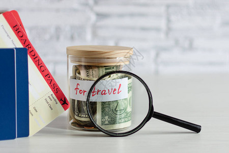 用放大镜和登机牌票在白砖墙上的白木桌上放着玻璃罐旅行的钱旅行预图片