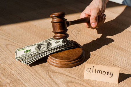 法官拿着木槌靠近美元钞票和桌子上写着赡养费的纸剪影图片