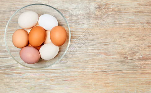 从白色到棕色的鸡蛋在木制桌子表面的玻璃碗图片
