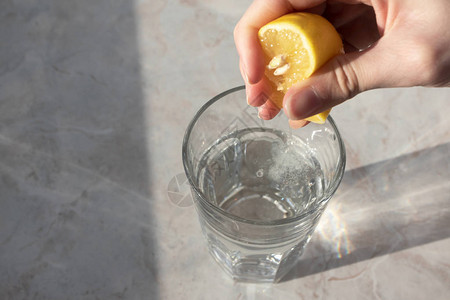 手在大理石桌背景上用苏打水在玻璃杯中挤柠檬汁排毒健康饮料概念图片