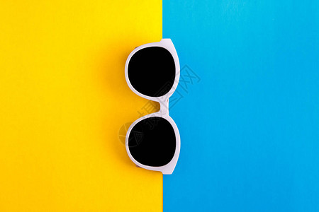 时尚的白色太阳镜在明亮蓝色和黄色橙背景上图片