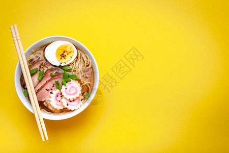 白色陶瓷碗中的美味日本面条汤拉面肉汤猪肉片火影忍者淡黄色背景的蛋黄图片