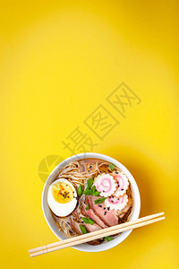 白色陶瓷碗中的美味日本面条汤拉面肉汤猪肉片火影忍者淡黄色背景的蛋黄背景图片
