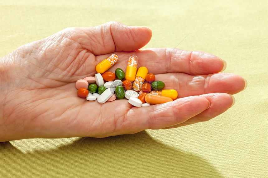 一位老妇人伸出手上的各种药片药丸和胶囊图片