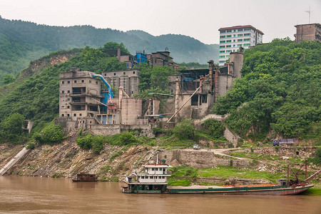 布朗石块破碎的工厂建在海岸线山上的绿色树叶间图片