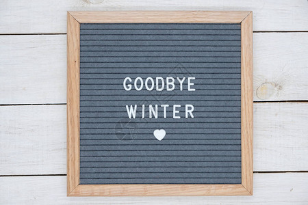 英文本再见冬天在信板上用灰色背景上的白色字母和心脏的象征白色木制背图片