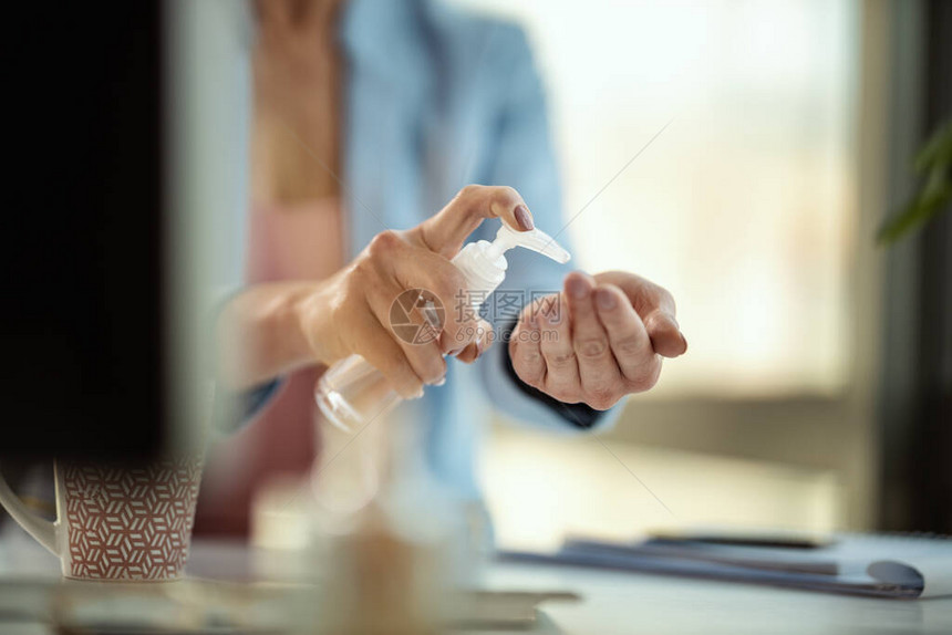 一位面目全非的女商人在自我隔离和检疫期间在电脑工作场所使用抗菌消毒凝胶进行手部消毒图片