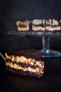 切片和巧克力蛋糕层与黄油奶坚果奶油和巧克力滴在深色木质背景的玻璃架上图片