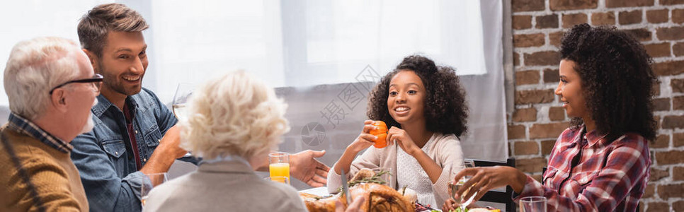在感恩晚宴期间坐在桌上美味的火鸡附近的多文化家庭图片