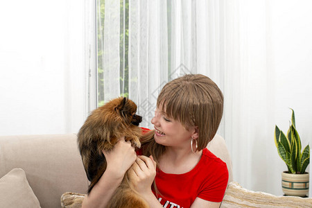 坐在沙发上抱着她宠爱的皮金色狗回家图片