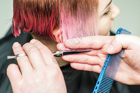 关闭一只阳刚的手正在用剪刀掉粉红色的头发将注意力集中在手和头发上美发图片