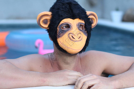 在游泳池中蒙猴子面具的英俊青年图片