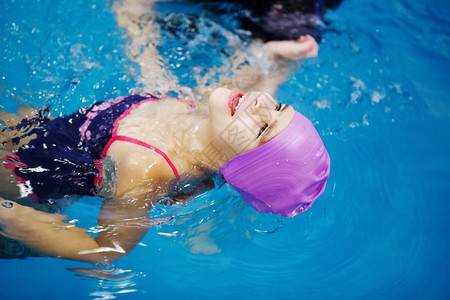戴着紫丁香帽的三岁孩子在男教练的帮助下在游泳池里游泳水疗水修复潜水健图片