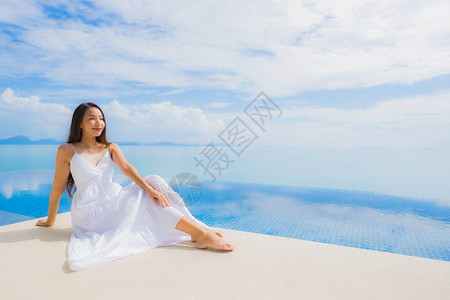 肖像年轻亚洲女在酒店和度假村的游泳池周围放松微笑图片