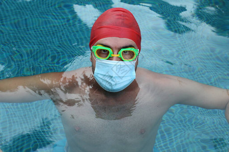 穿着医疗保护面罩和游泳护目镜的英俊青年男子在冠状封闭期间在泳池中图片