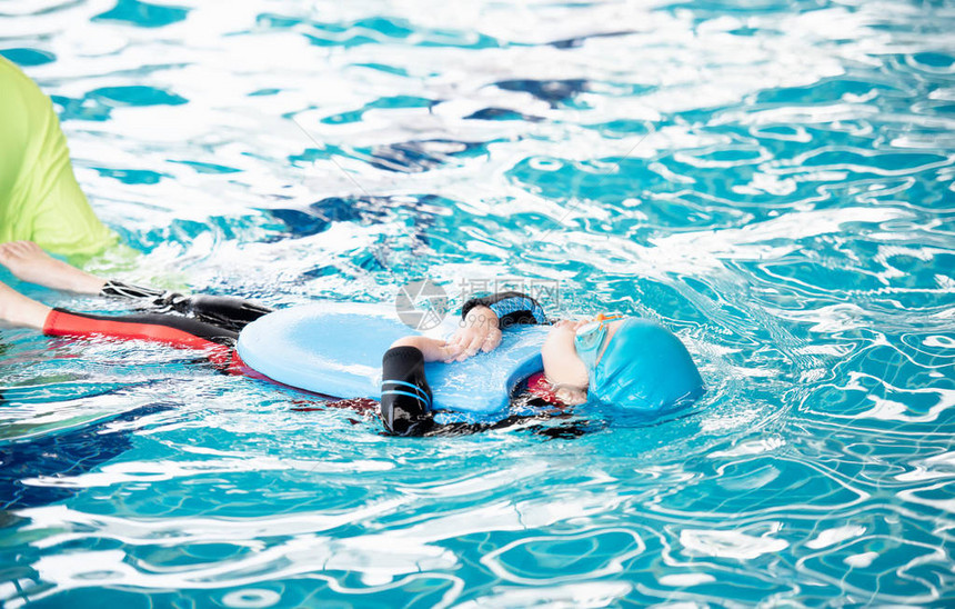 一个穿着泳衣的女孩用泡沫垫和老师在游泳池里练习游泳图片