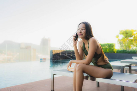 在酒店度假村室外游泳池周围的床上使用手机拍摄美丽的亚洲图片