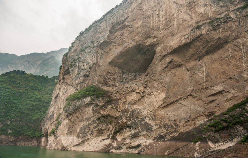 长江西泠峡谷棕色岩石悬崖上的大洞在绿水中下降绿色覆盖的山脉作为背景一图片