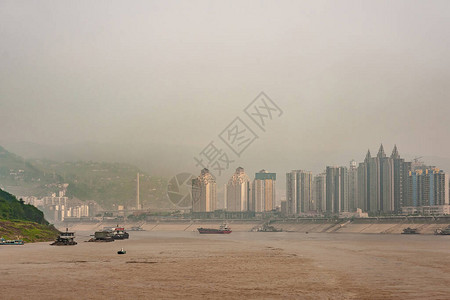 长江在几艘船上的棕色水岸上有高楼的城市景观雾和图片