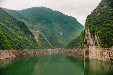 深峡谷充满翠绿的水在绿色森林覆盖的山脉和靠近水的棕色岩背景图片