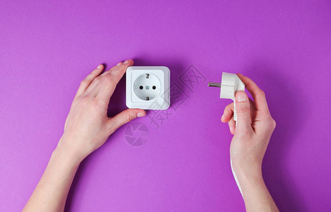女手将电源插头入紫色背景的电源插座极简主义图片