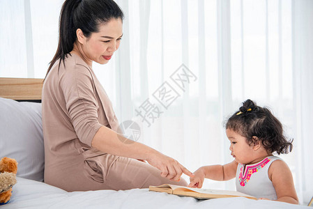 亚洲母亲教女孩儿在家看书家庭概念中的隔离快图片