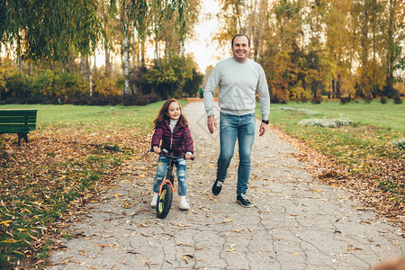 快乐的父亲和女儿带着自行车在公园中走动图片