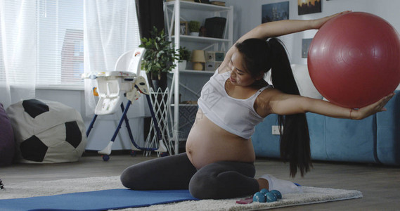 一名年轻孕妇在用健身球训练时观看辅导录像图片
