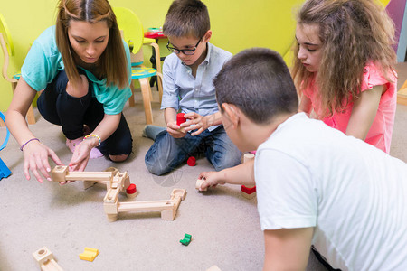 一位专职幼儿园教师在有监督的游戏时间帮助孩子们建造木制火车背景图片
