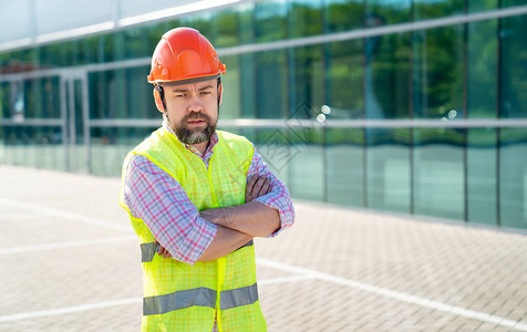 穿着背心和防护头盔的男工头或建筑检查员站在新结构的背景上专图片