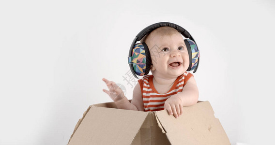 白色背景下戴着迪斯科耳机的盒子里的可爱女婴图片
