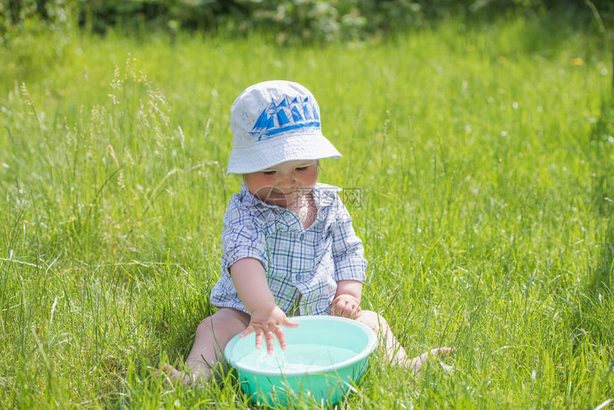 孩子在草地上玩一盆水有趣的男婴在外面玩水和泡一个可爱的小男孩在外面的浴缸里玩泡肥皂和水时图片