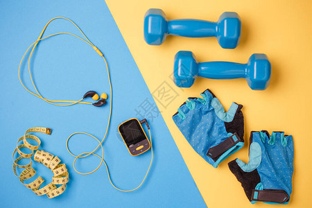 玩家哑铃瓶水厘米胶带蓝和黄色背景的手套图片