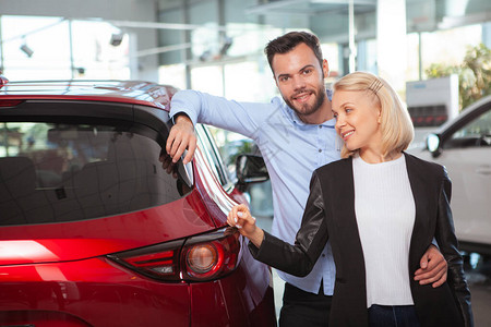 快乐的情侣在经销商的新车旁边拥抱着幸福的一对情侣爱情旅行图片