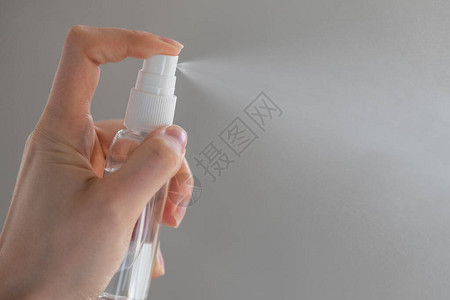 女或女孩在手部使用喷雾消毒酒精产品消毒手部以防止灰色背景下的图片