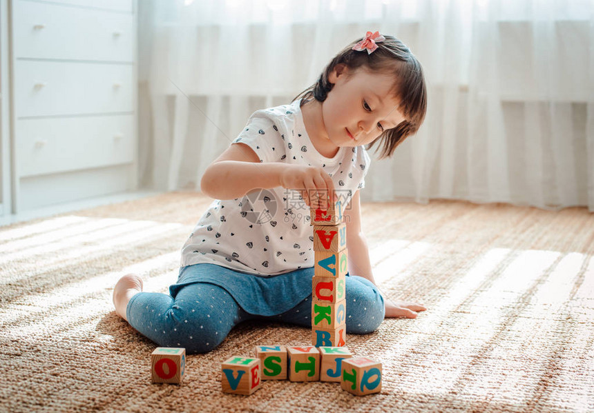 岁的孩子在房间的地板上玩带有彩色字母的木制立方体图片