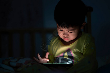 闭眼小男孩正在床上看平板电脑上的视频图片
