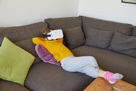 六岁小孩躺在棕色沙发上在家看虚拟现实耳机眼镜图片