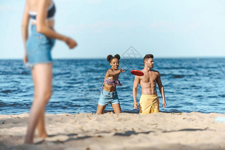 在沙滩上玩飞盘的种族间朋友有选择地聚焦于沙滩图片
