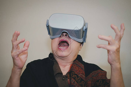 身戴虚拟现实护目镜的年老亚洲老年妇女V背景图片