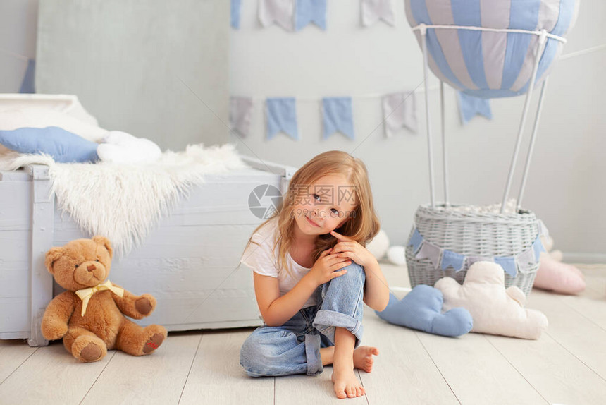 穿着白色T恤和牛仔裤的微笑小女孩坐在装饰气球的背景上孩子在儿童房玩耍童年的概念生日图片