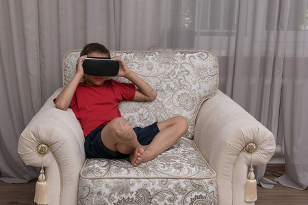 戴虚拟现实眼镜的男孩坐在大扶手椅上图片
