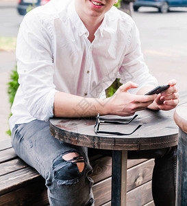 照片中一名身着白衬衫和牛仔裤的年轻人坐在咖啡厅的桌子上图片