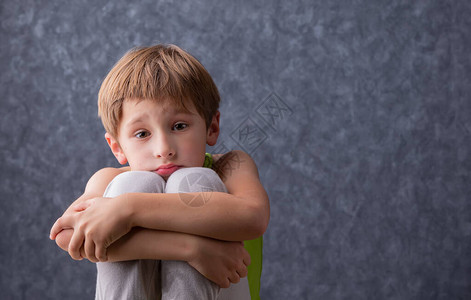 一个悲伤的孩子抱着膝盖坐着一个小学年龄的男孩很伤心小学生在灰图片