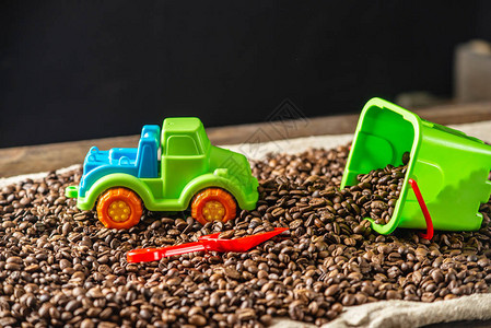 孩子们的明亮玩具是一个带铲子的水桶和一辆放在一堆烤咖啡豆上的汽车图片