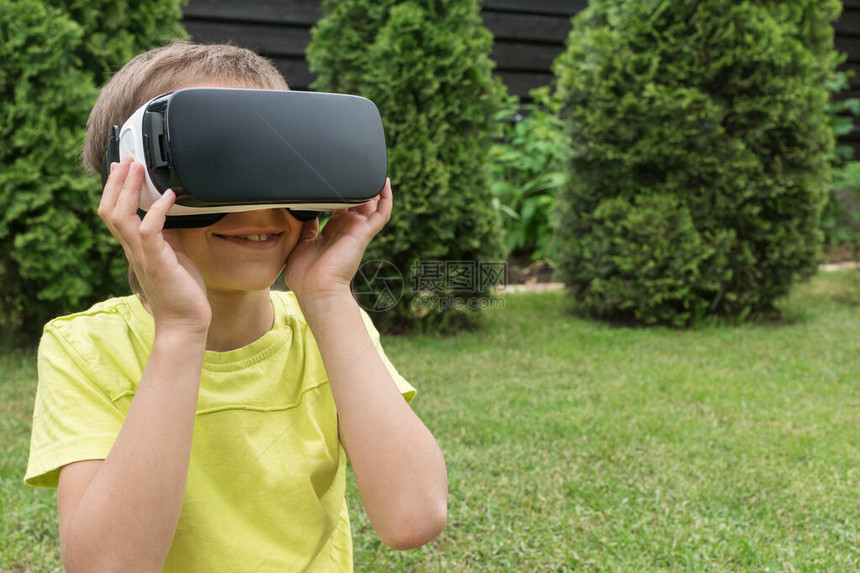 在绿色公园外面戴着虚拟现实眼镜的男孩在网络空间里看着一些非常有趣的东西并微笑着复制文本的空间新技术图片