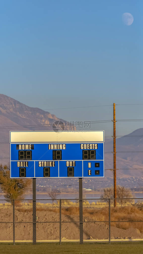在运动场的垂直的蓝色和白色电子棒球记分牌在背景中可以看到蓝天下的湖泊山谷图片