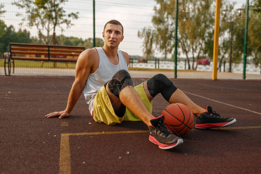 有球的篮球运动员坐在室外球场的地上街球训练后穿着运动服的图片