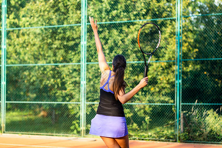 年轻女子在室外网球场练习发球图片