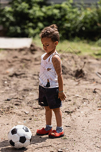 身着肮脏衣服站在城市街足球场附近的非洲可怜男孩图片
